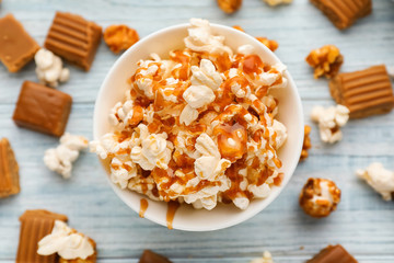 Bowl full of delicious popcorn with caramel on wooden background, top view