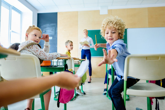classmates passing message during lesson while teacher looking at them