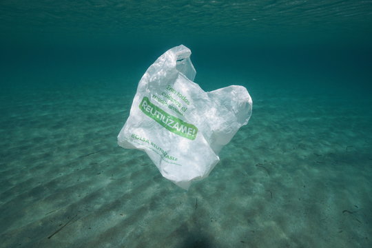 Plastic pollution underwater, a bag with text in Spanish "together we take care of the environment, reuse me, reusable bag" adrift in the Mediterranean sea, Almeria, Andalusia, Spain
