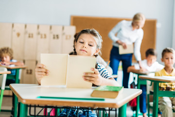adorable little schoolgirl reading book during lesson