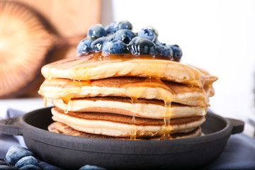 Frying pan with tasty pancakes, honey and blueberries, closeup