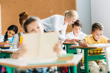 smiling teacher helping children with work during lesson