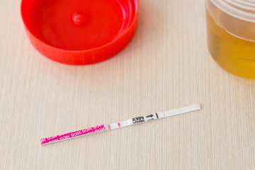 Positive pregnancy test result with two strips on the table. Next to the urine can.
