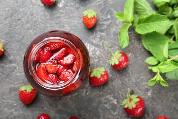 Glass jar with delicious strawberry jam on grunge table