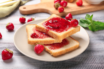 Plate with slices of bread and delicious strawberry jam on wooden table