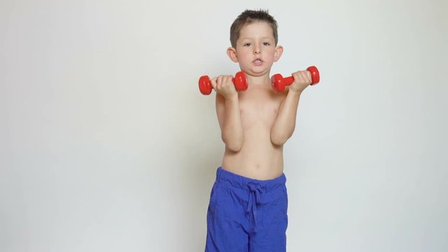 Smiling boy is doing exercises with dumbbells on the white background