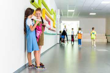 two happy schoolgirls chatting at school corridor during break