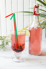 A cup of summer plum lemonade with straw. Decanter with compote. Decor of a green flower. Rustic. White wooden background.