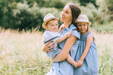 Fototapeta premium beautiful mother hugging two kids in straw hats in field