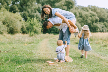 Fototapeta premium happy family with two kids spending time on summer feild, father piggybacking mom