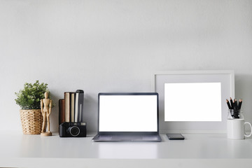 Mockup Laptop on workspace and camera film, photo frame, book, jar of pencil with tree decoration office desk.