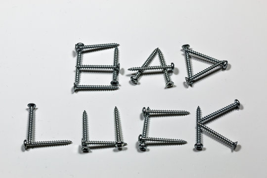 The word bad luck written with screws on a white background with reflections
