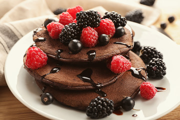 Tasty chocolate pancakes with berries on plate, closeup