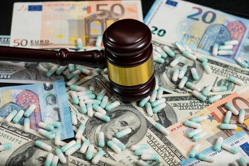 Wood judge's gavel and scattered colorful drugs on the dollar and euro cash background
