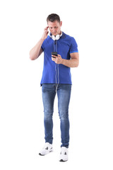 Adult casual man scratching head searching for music on smartphone wearing earphones. Full body isolated on white background. 