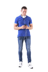 Young adult man with headphones around neck browsing music on smart phone app. Full body isolated on white background. 