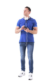 Thinking adult casual man with earphones attached to smartphone looking up. Full body isolated on white background. 