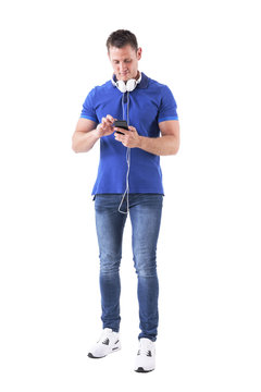 Adult casual man with headphones typing on smart phone touch screen searching for music. Full body isolated on white background. 