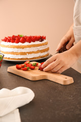 Woman preparing delicious cake with strawberries at table