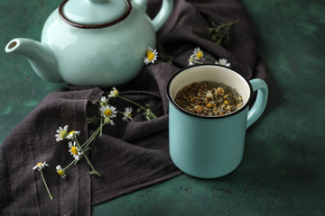 Cup and teapot with delicious camomile drink on green table