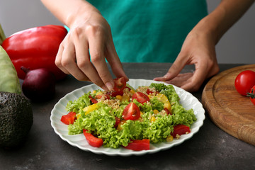 Woman preparing healthy salad on grey table, closeup