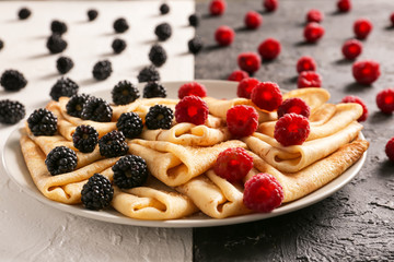 Plate with tasty thin pancakes and berries on table, closeup