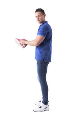 Profile view of young adult man holding and buying sport sneakers looking at camera. Full body isolated on white background. 