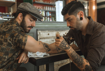 Artist tattooing man's arm in a bar