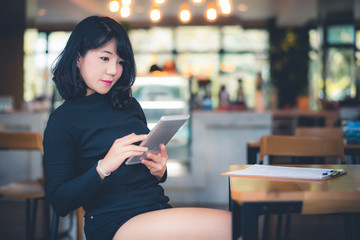 Beautiful attractive young Asian woman using smart phone or cellphone or tablet at cafe in the morning 