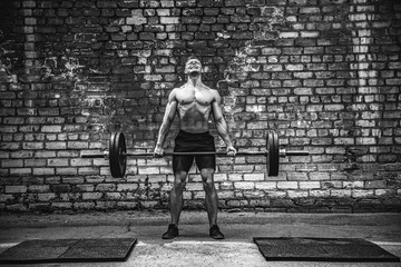 Muscular fitness man doing deadlift a barbell over his head in outdoor, street gym. Functional...