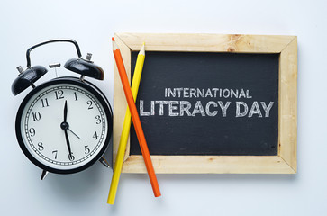 International Literacy Day. Alarm Clock, Color Pencil and Blackboard on White Background