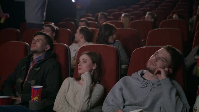 Young people enjoying film in cinema. Noisy company of guys coming to movie show late. Boorish people interrupt session. People indignantly look at late guys in cinema. Uncultured guy at cinema watch