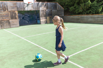 Ein 7 jähriges Mädchen trainiert mit einem Fußball auf einem Bolzplatz mit grünem Spielfeld