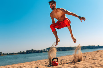 Fototapeta na wymiar Young man doing fitness workout at a beach on a sunny day. Bare chested man running and jumping.