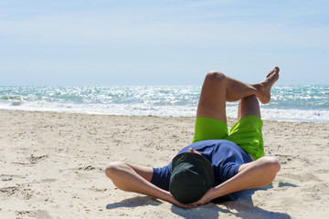Young man traveler with hat on face sleeping with happiness and relaxing on beautiful beach.