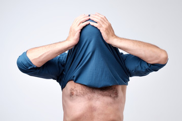 Man hiding his face with undershirt. Human hid head with t-shirt