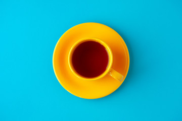 Yellow tea cup on a blue background. View from above. A bright yellow tea pair on a blue background creates a contrast.