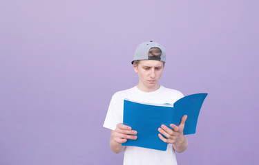 Young student in a white T-shirt read a book on a purple background. A student stands with a magazine on the background of a purple wall and reads. Learning the concept. isolated