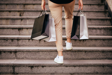 Close up of woman`s legs climbing the stairs. In hands paper bags for shopping.