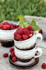 Summer still life, cups full of ripe raspberries. August, September background.