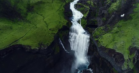 Top down aerial view of giant waterfall flowing in Iceland mountains filmed in slow motion