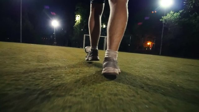 Man in sneakers walks to the ball and puts his foot on the ball, night shooting on the football field