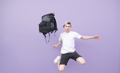 Man in a white T-shirt jumping with a backpack on a purple background.Backpack and a man flying...