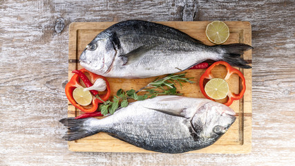 Web banner. Dorado on a cutting board on a wooden table. Herbs, lime, cherry tomatoes, salt, paprika and spices. Top view. Copy space