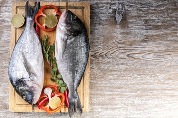 Dorado on a cutting board on a wooden table. Herbs, lime, cherry tomatoes, salt, paprika and spices. Top view. Copy space