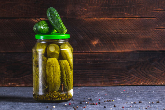 Glass jar of pickled homemade, fresh cucumbers on a dark, wooden background. Copy space