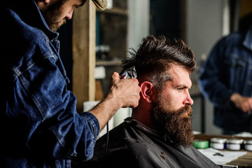 Barber with hair clipper works on hairstyle for bearded man barbershop background. Barber styling...