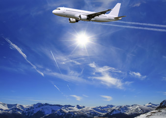 Fototapeta na wymiar Airplane flying over sunny blue sky and Alpine mountains background