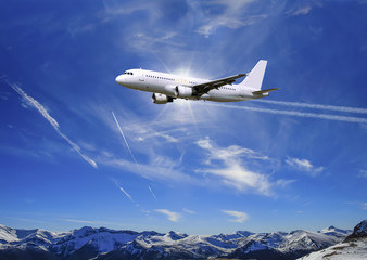 Fototapeta na wymiar Airplane flying over sunny blue sky and Alpine mountains background