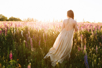 Young woman standing on a wheat field with sunrise on the background
